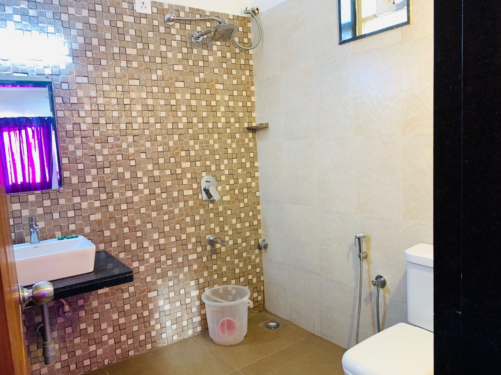 A bathroom with a tiled shower wall, a sink with a mirror, and a toilet.