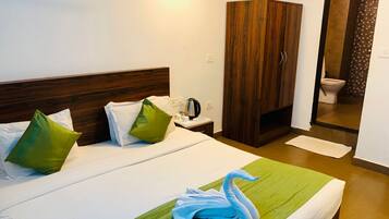 Ein Hotelzimmer mit einem Bett, grünen und weißen Kissen, einem Holzschrank, einem Nachttisch mit einem Wasserkocher und einem zu einem Schwan geformten Handtuch.
