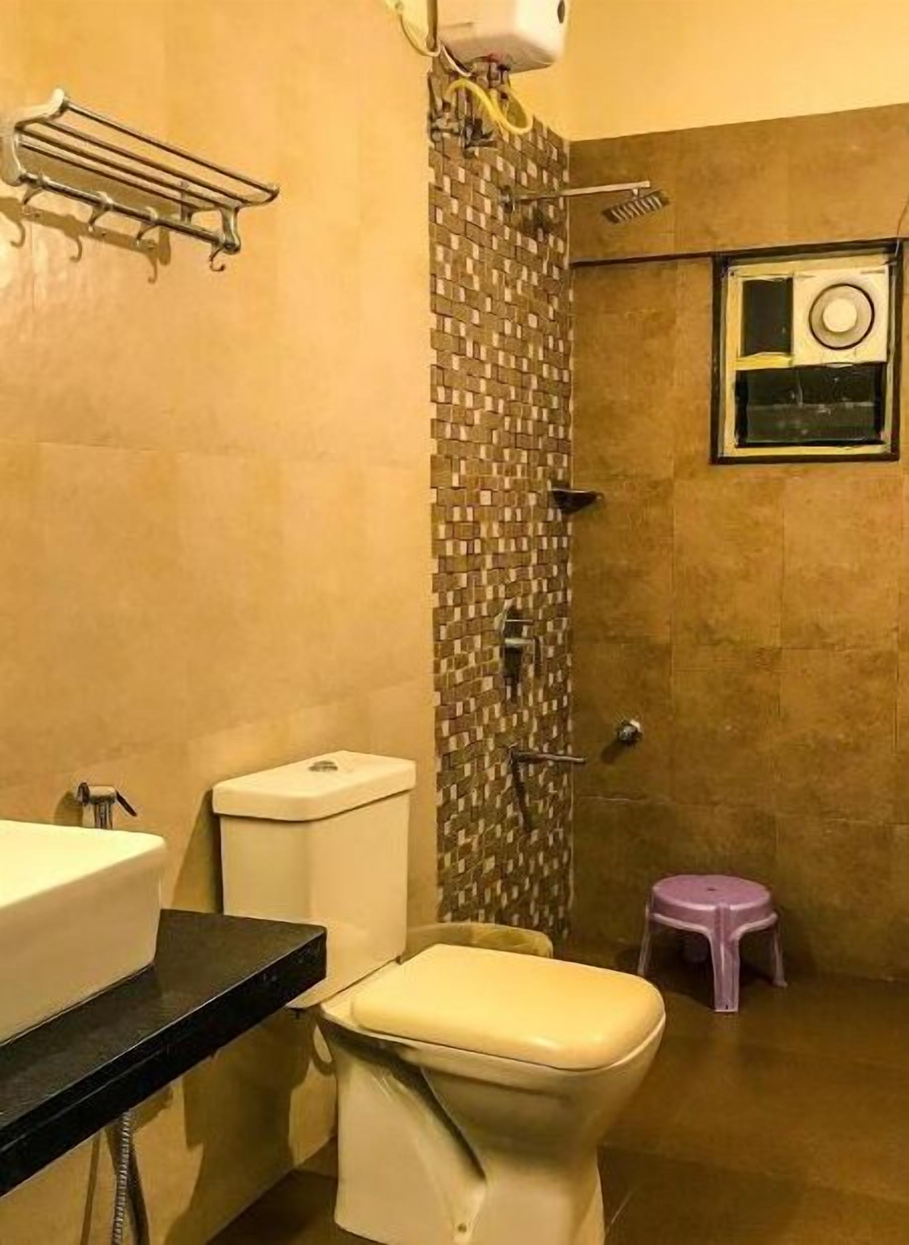Un baño con inodoro, lavamanos, ducha y un taburete pequeño.