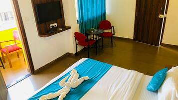 A hotel room with a bed, a TV mounted on the wall, a dining area with a table and chairs, and a door.