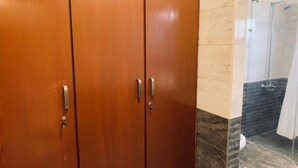 Une armoire en bois à deux portes, dotée d’un trou de serrure, située à côté d’un espace douche avec une porte en verre.