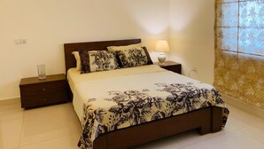 Une chambre à coucher avec un lit, des tables de chevet, une lampe et une fenêtre ornée de rideaux à motifs floraux.