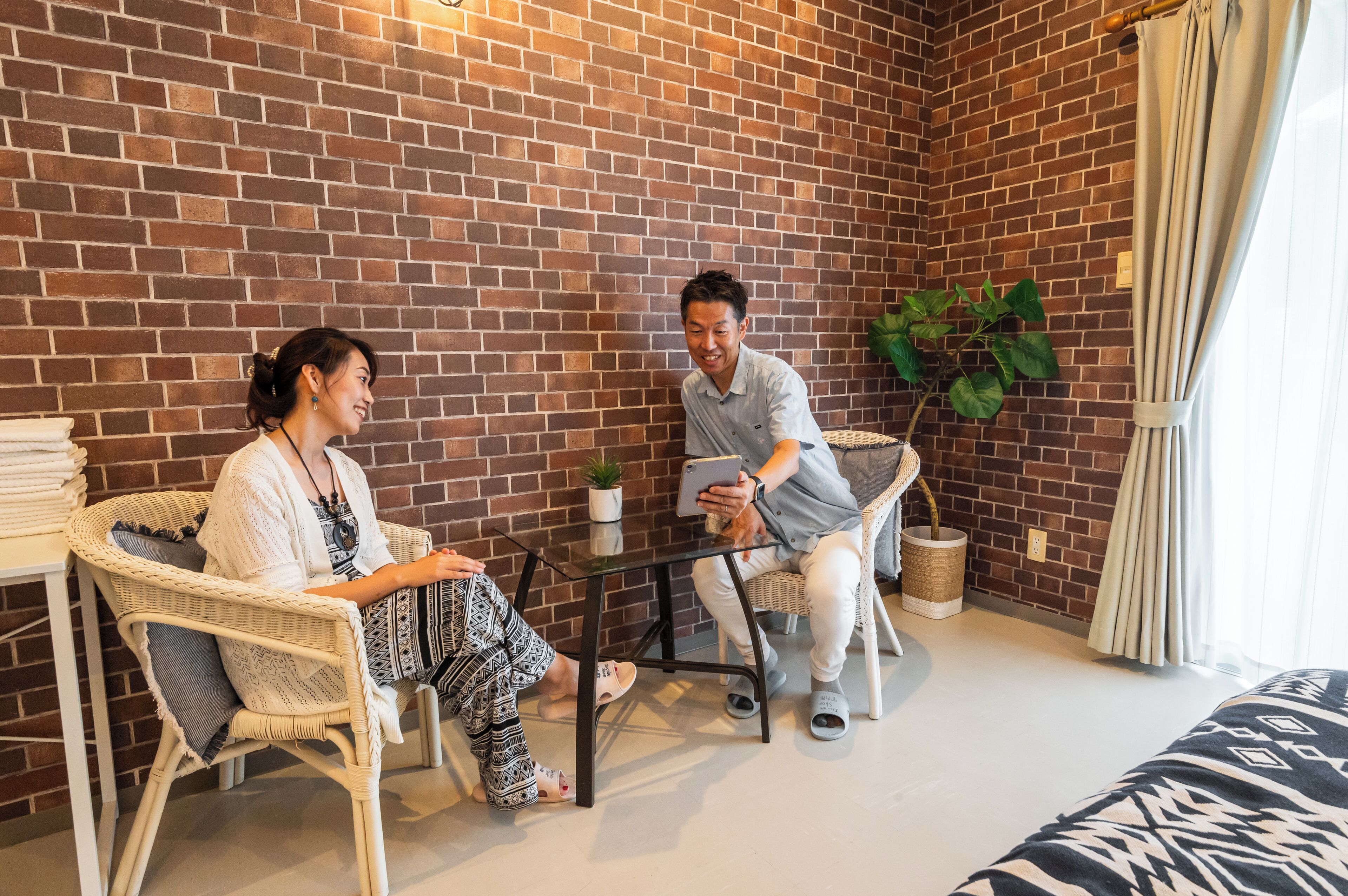 A cozy room with a brick wall, wicker chairs, a glass table, and a potted plant.