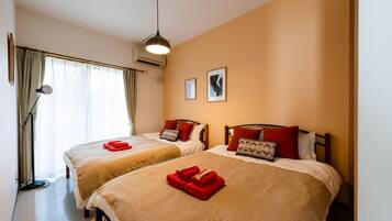 A hotel room with two beds, each with red towels, a standing lamp, and framed pictures on the wall.