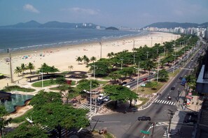 Une plage bordée d’une route qui la longe, avec des palmiers et des lampadaires plantés le long de celle-ci.