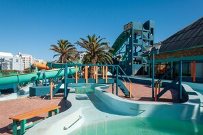 Um parque aquático com toboáguas e área de piscina, cercado por palmeiras e edifícios.