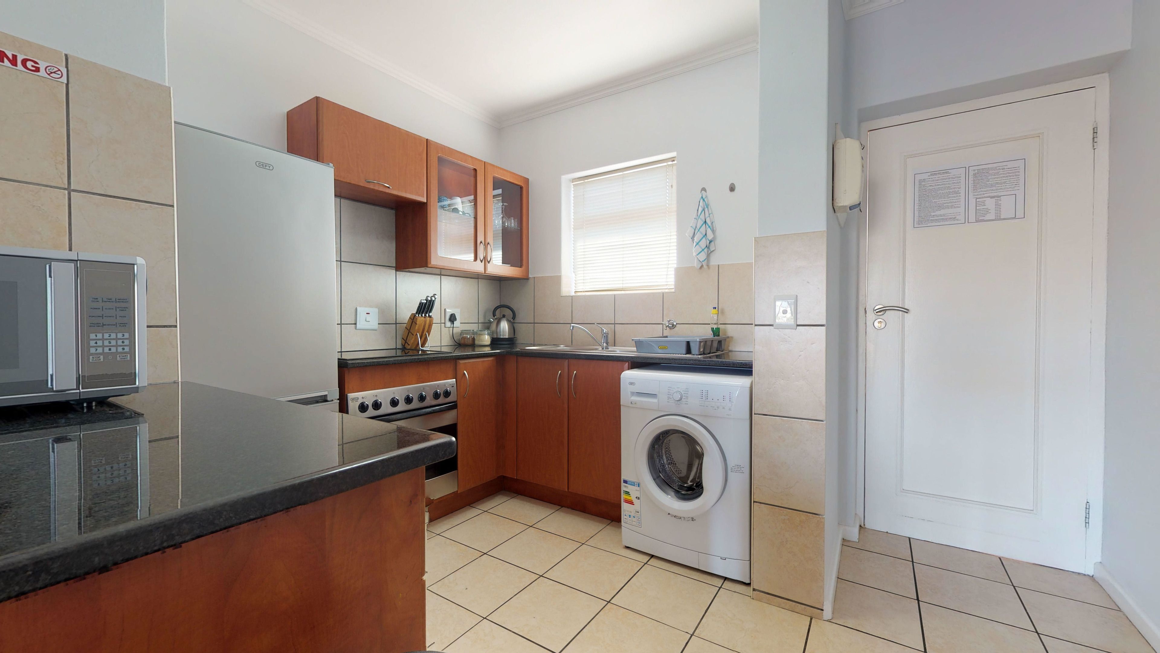 A compact kitchen with a microwave, oven, and washing machine.