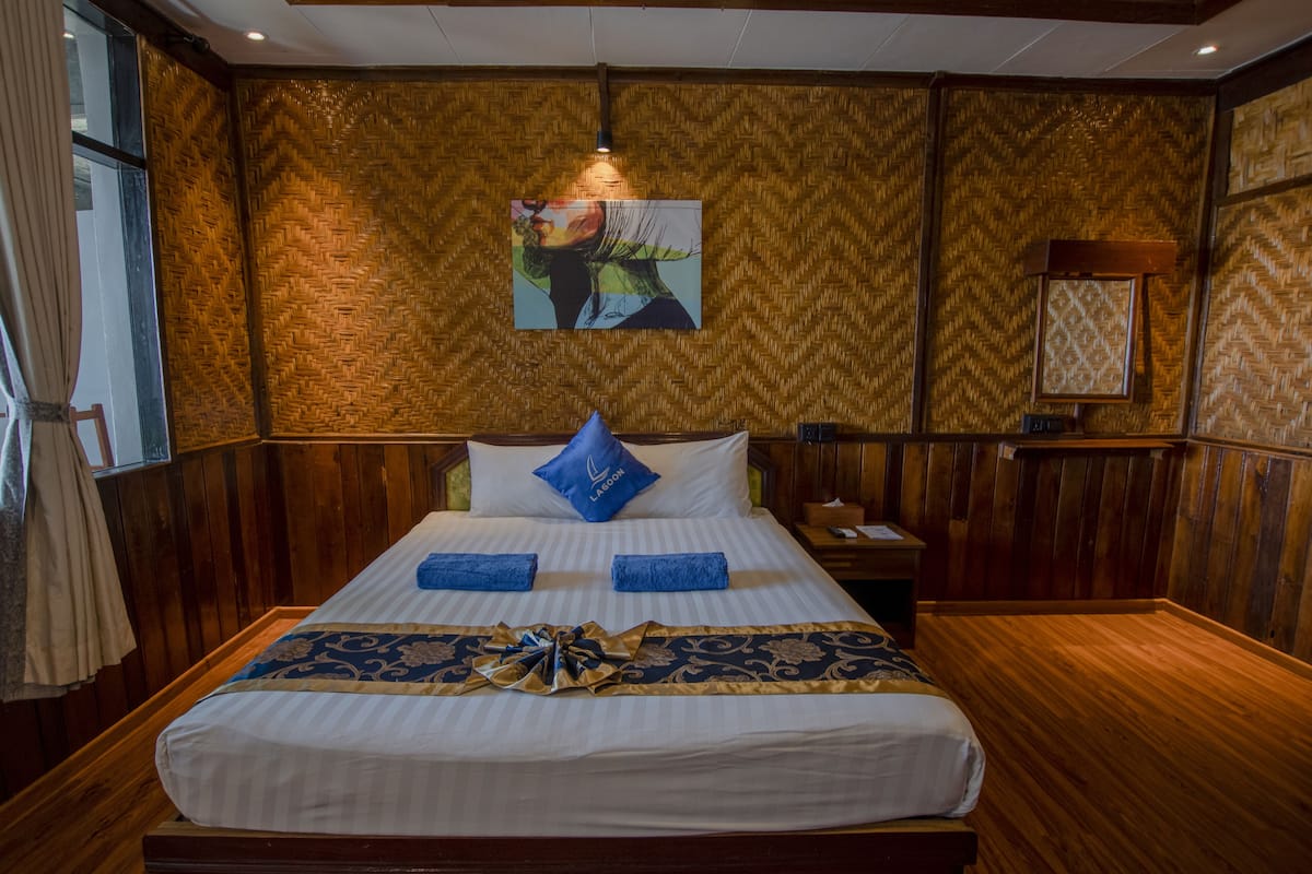 Een hotelkamer met een groot bed, houten lambrisering, een schilderij aan de muur en een nachtkastje met een lamp.