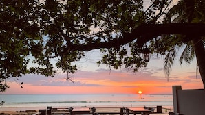 Ein Restaurant direkt am Strand mit Außenbereich und Blick auf den Ozean bei Sonnenuntergang.