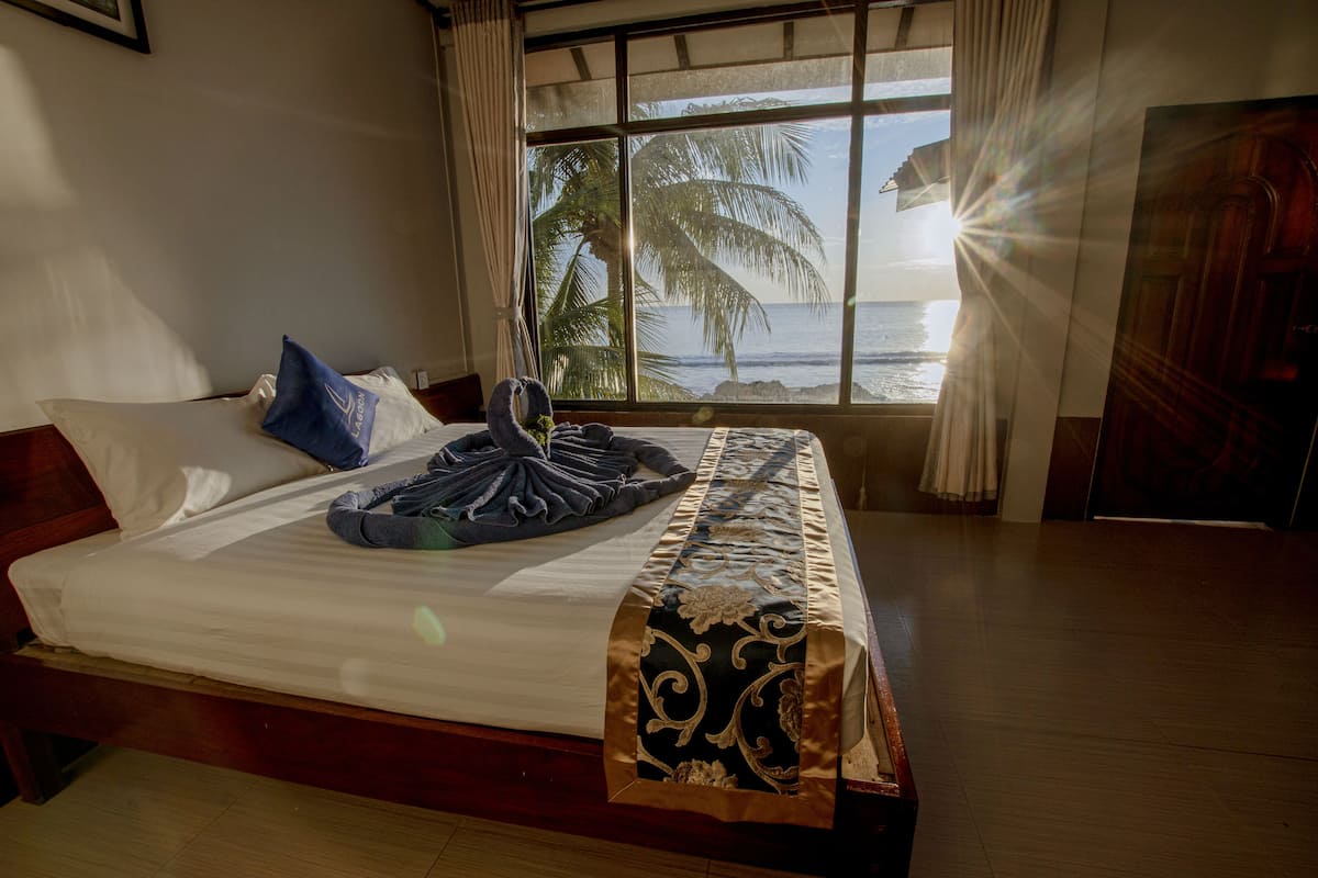 Een hotelkamer met een bed, een raam met uitzicht op de oceaan, en een houten vloer.