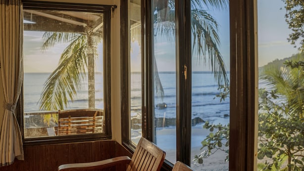 Ein Zimmer mit großem Fenster und Meerblick, ein Holzstuhl und ein Vorhang.