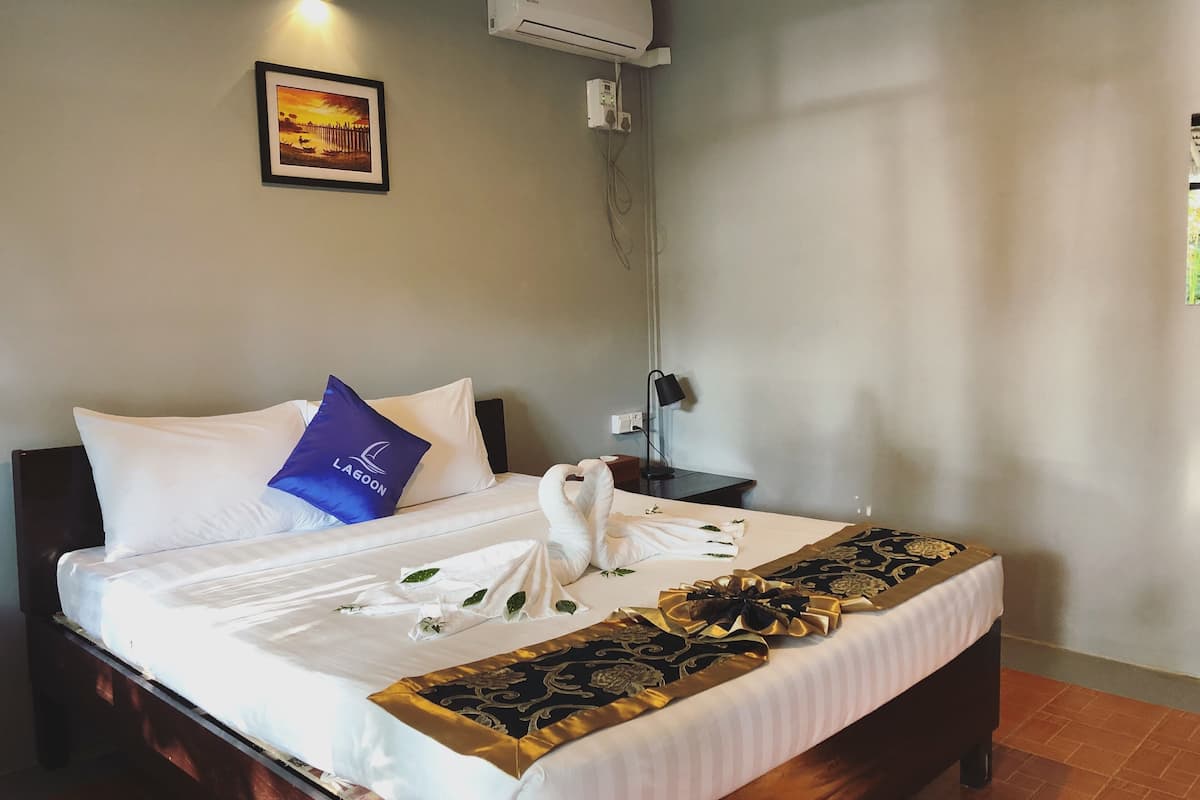 Een netjes opgemaakt bed met een witte deken, een blauw kussen met de tekst 'LAGOON' en een decoratieve gouden en zwarte loper.