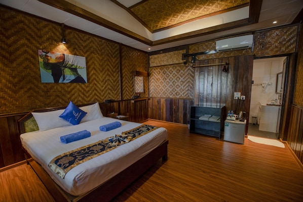 A hotel room with a large bed, wooden walls, a painting, and a small kitchenette.