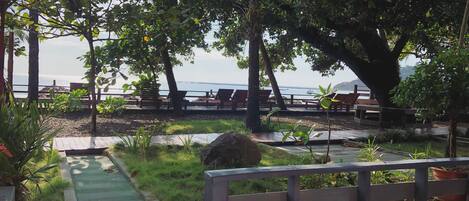 Un patio frente a la playa con asientos de madera y un sendero que lleva a la arena.