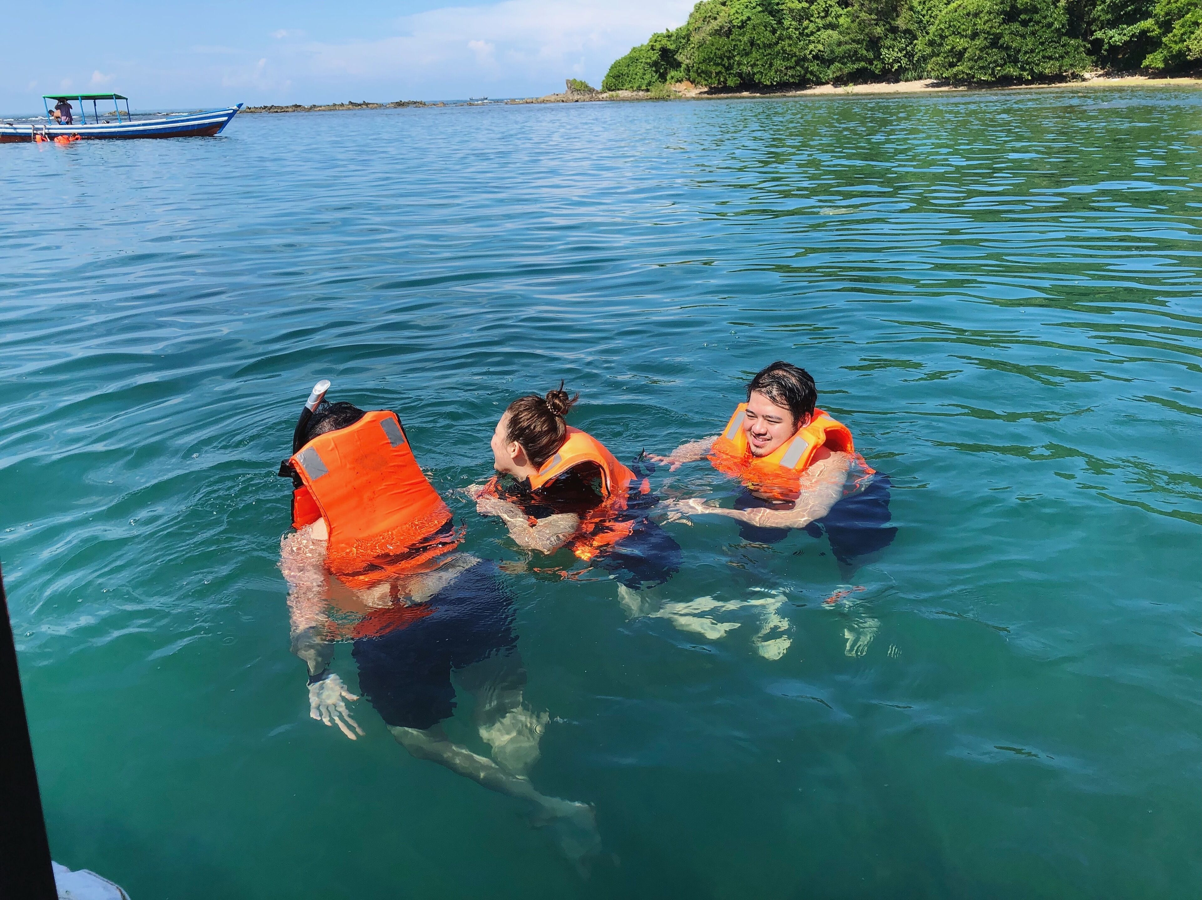 Three people in a boat wearing life jackets.