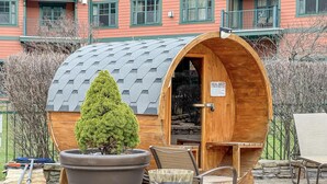 Eine Sauna mit Holzfassade, einem großen Topfpflanzen, Steinsitzen und einem Schild mit Sicherheitsanweisungen.