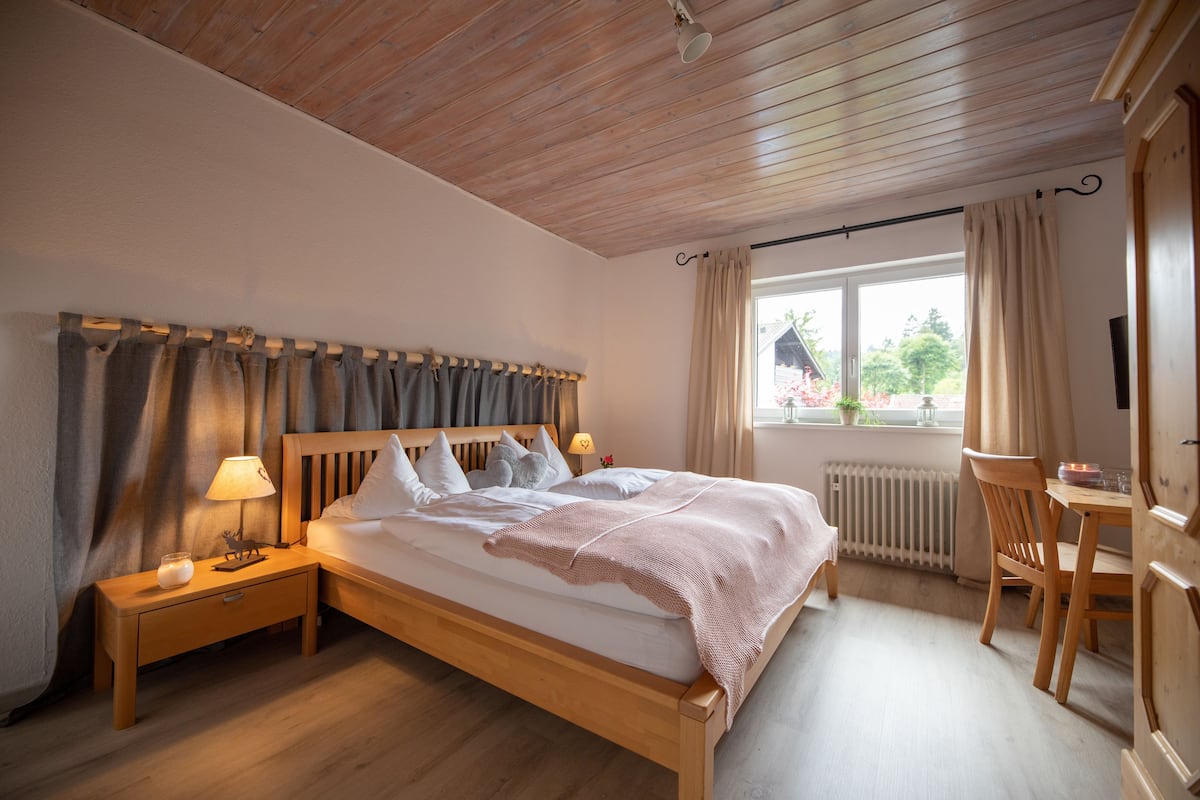Quarto com cama de madeira, mesas de cabeceira, luminária, janela com cortinas, radiador e uma cadeira.