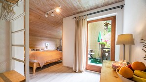 A bedroom with a bed, a wooden bench, a table with fruit, and a view of the outdoors. - Gästehaus Richter (Grainau)