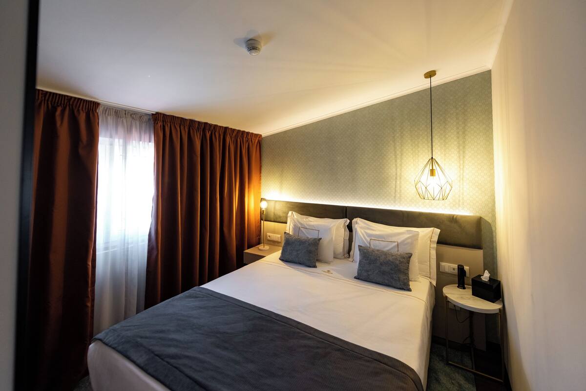 Une chambre d’hôtel avec un lit, des tables de chevet, une lampe et une fenêtre avec des rideaux.
