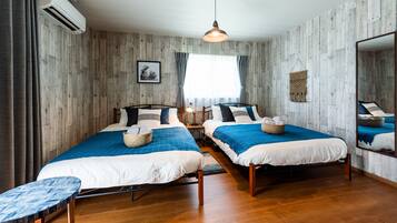 A room with two beds, wooden flooring, a hanging light fixture, and a large mirror.