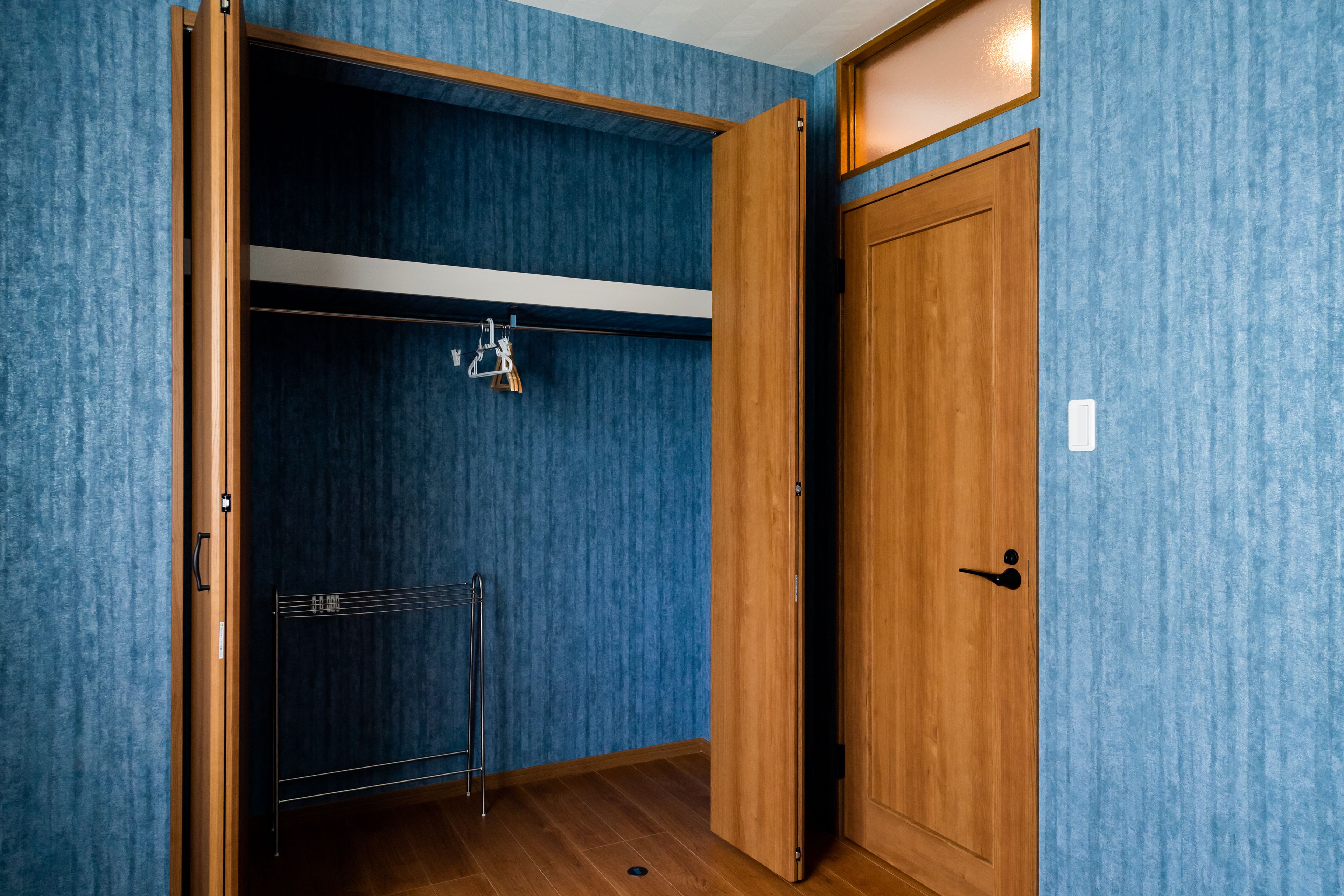 A room with a wooden wardrobe, a metal rack, and a blue textured wall.