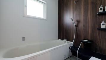 A modern bathroom with a large bathtub, a shower, and a window.