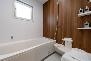 Enjoy a refreshing soak in the bathtub with showerhead, adjacent to a toilet and wall-mounted bidet.
