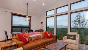 Ein geräumiges Wohnzimmer mit einer Ledersofa, einem Holztisch und Blick auf eine grüne Landschaft durch große Fenster.