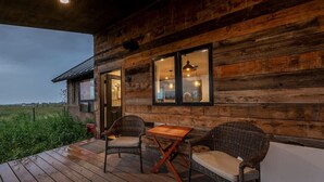 Eine Holzhütte mit einer Terrasse, zwei Korbstühle, einem kleinen Tisch und einer Hängelampe.