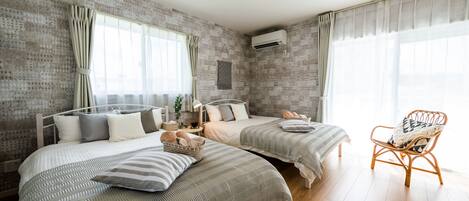 Un dormitorio moderno con dos camas, una silla de mimbre y un ventanal grande.