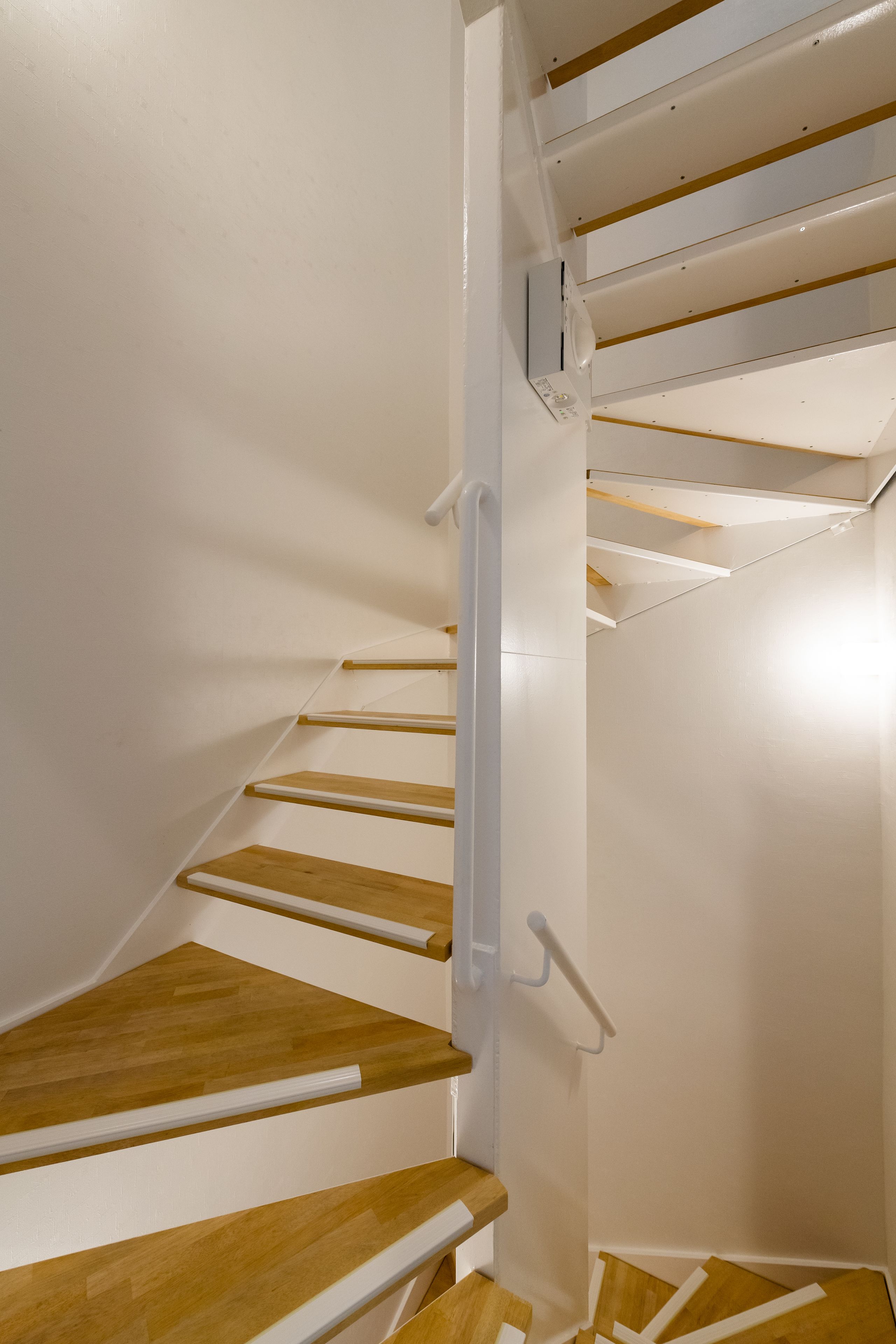 A spiral staircase with wooden steps and white handrails, leading to an upper floor.