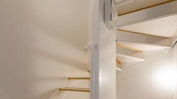 A spiral staircase with wooden steps and white handrails, leading to an upper floor.