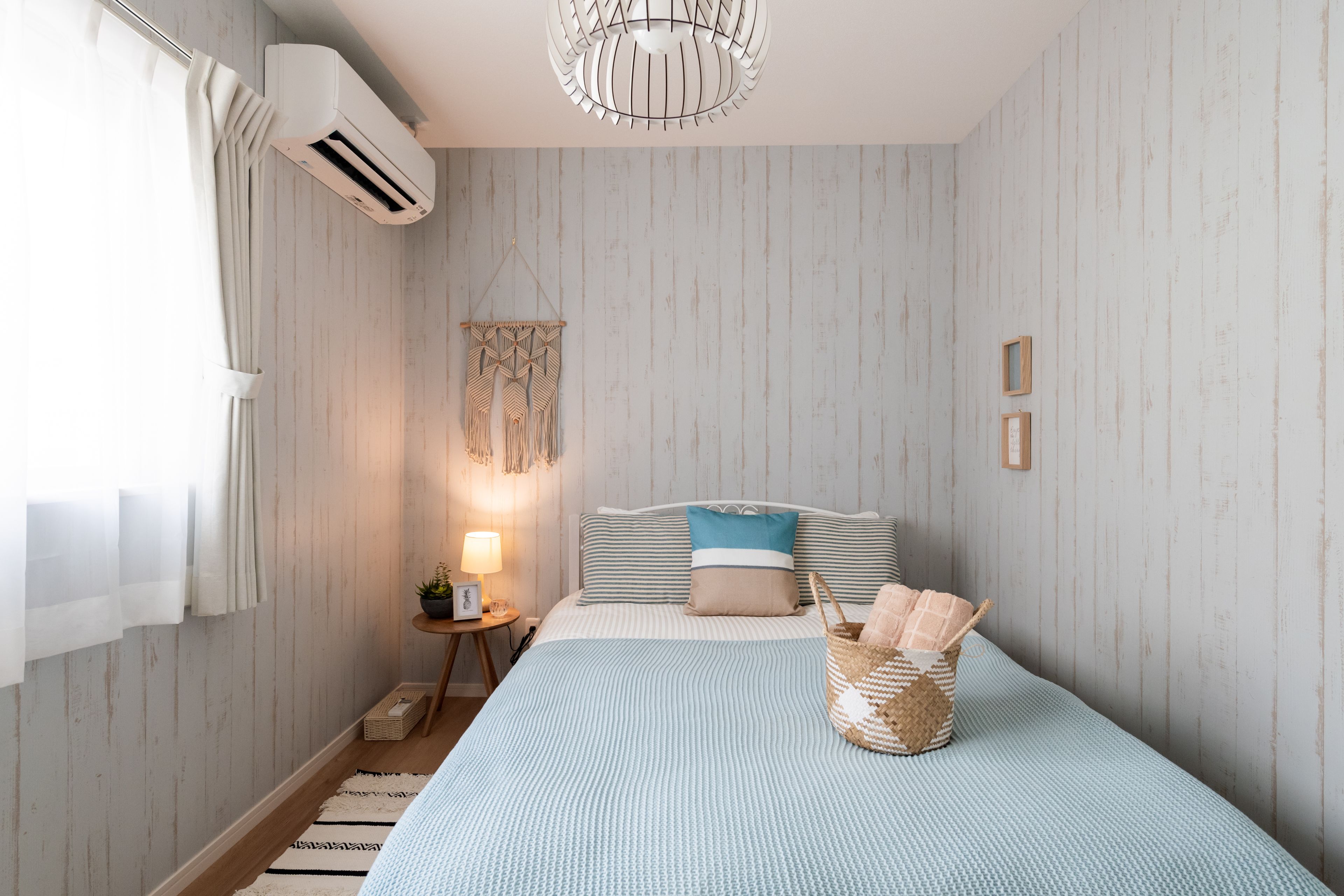 A bedroom with a bed, bedside table, lamp, air conditioning unit, and a wall-mounted light fixture.