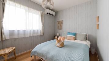 A bedroom with a bed, a wicker chair, a hanging macrame wall decoration, and an air conditioning unit.