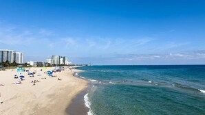 A beach with clear blue water, sandy shore, and buildings in the background. - Kanda Zen Apt 3 - pool & walk to the beach! (Pompano Beach)