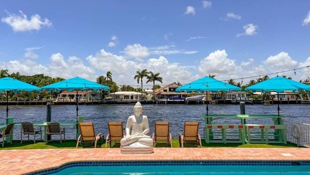 A pool area with a Buddha statue, lounge chairs, and blue umbrellas. - Kanda Zen Apt 3 - pool & walk to the beach! (Pompano Beach)