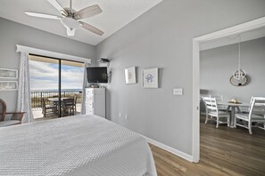 A bedroom with a large bed, a ceiling fan, a TV, and a balcony with a table and chairs. - Phoenix V 110 by Liquid Life (Orange Beach)