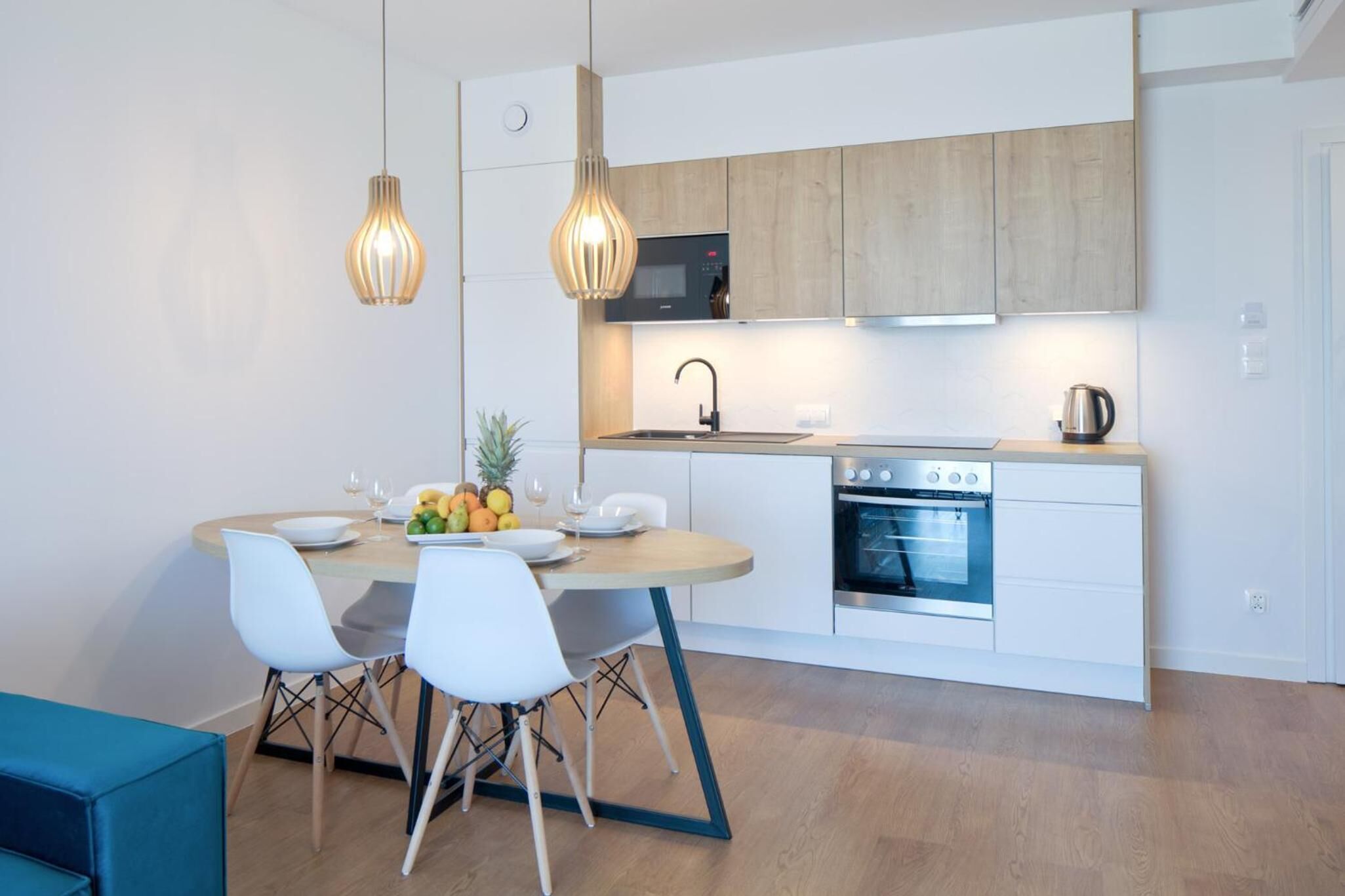Een moderne keuken met witte kastjes, een inbouwoven en een eethoek met een ronde tafel en stoelen.