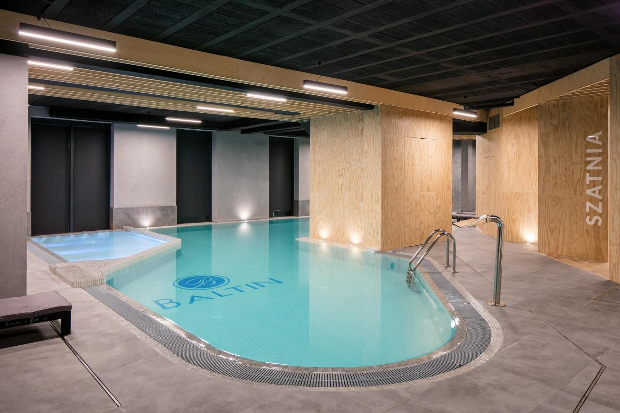 En swimmingpool med træbeklædning, med teksten "BALTIN", og et saunaområde med et synligt logo.