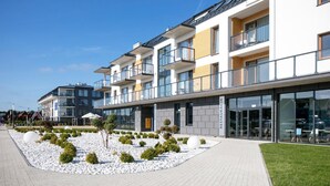 A modern multi-story building with balconies, a restaurant, and a landscaped area with white gravel and shrubs. - Blu Apartments (Sarbinowo)