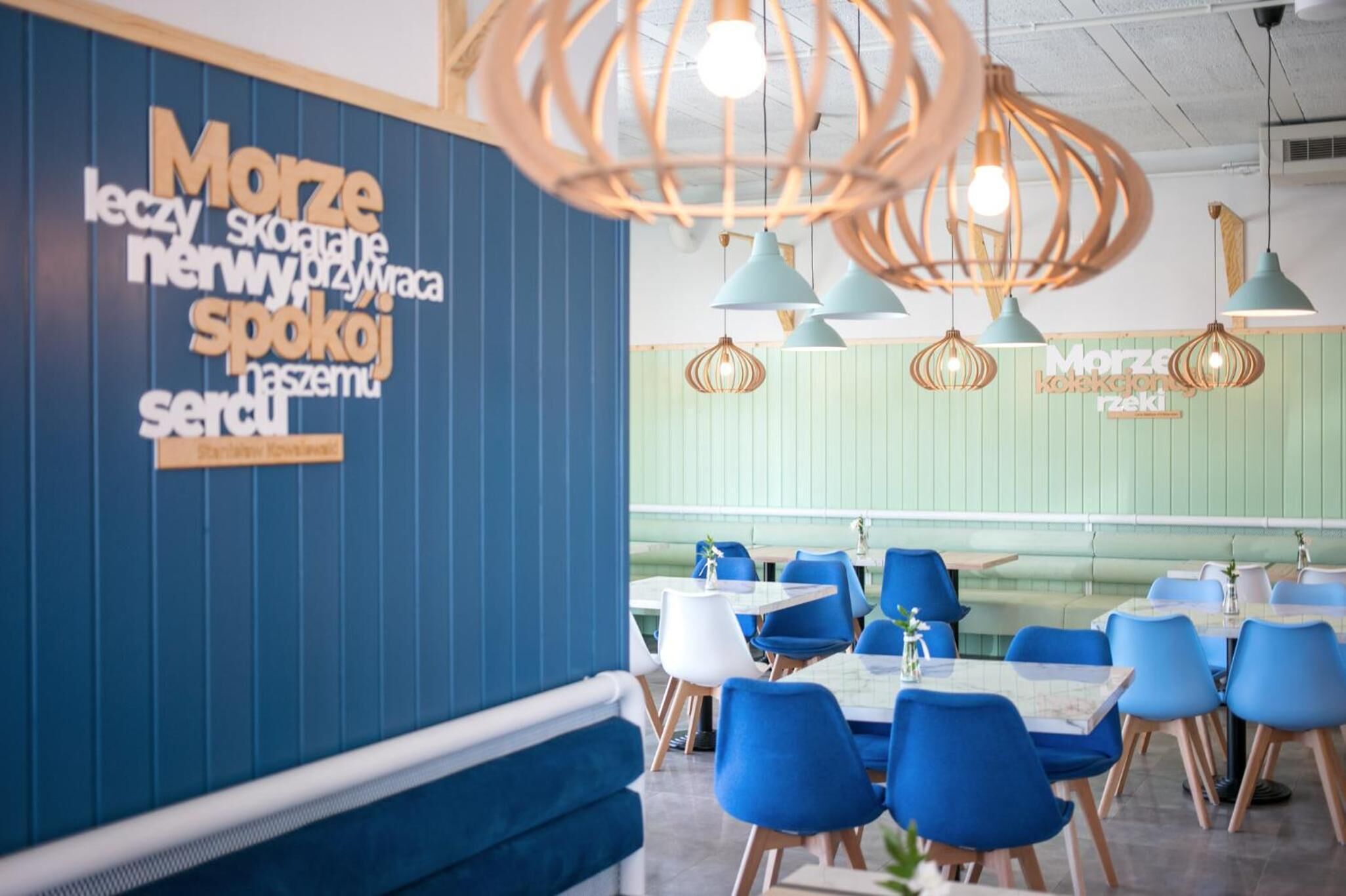 A restaurant interior with blue and white chairs, wooden tables, and hanging pendant lights.