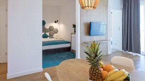 A modern hotel room with a bed, a TV, a dining table with fruit, and a large window. - Blu Apartments (Sarbinowo)