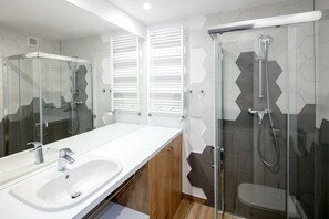 Een moderne badkamer met een douchecabine van glas, een grote spiegel en een witte wasbak.