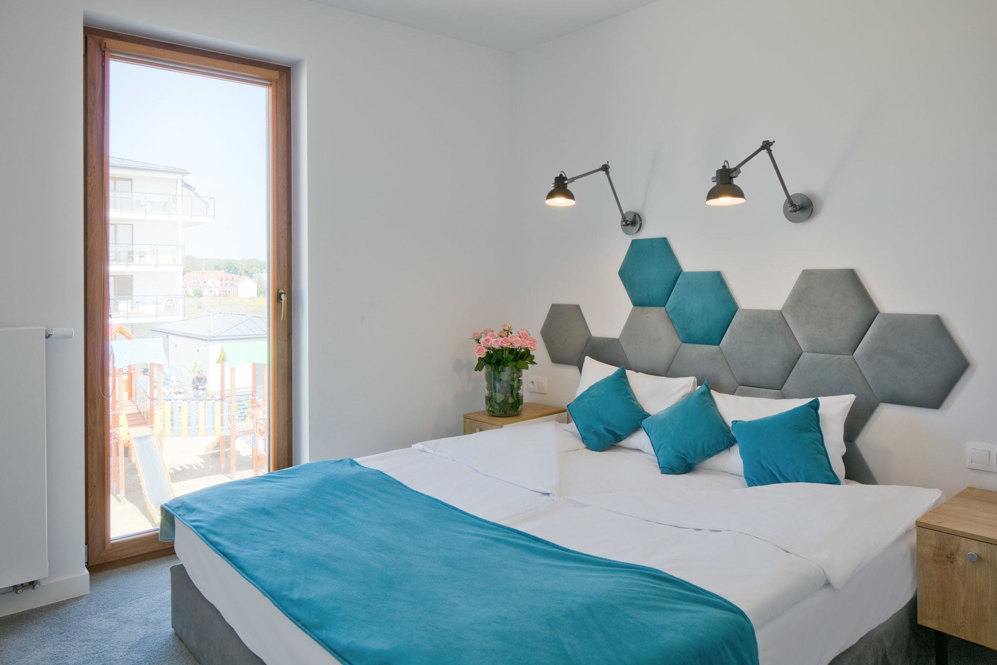 Een slaapkamer met een bed, een nachtkastje, een wandlamp en uitzicht door een deur.