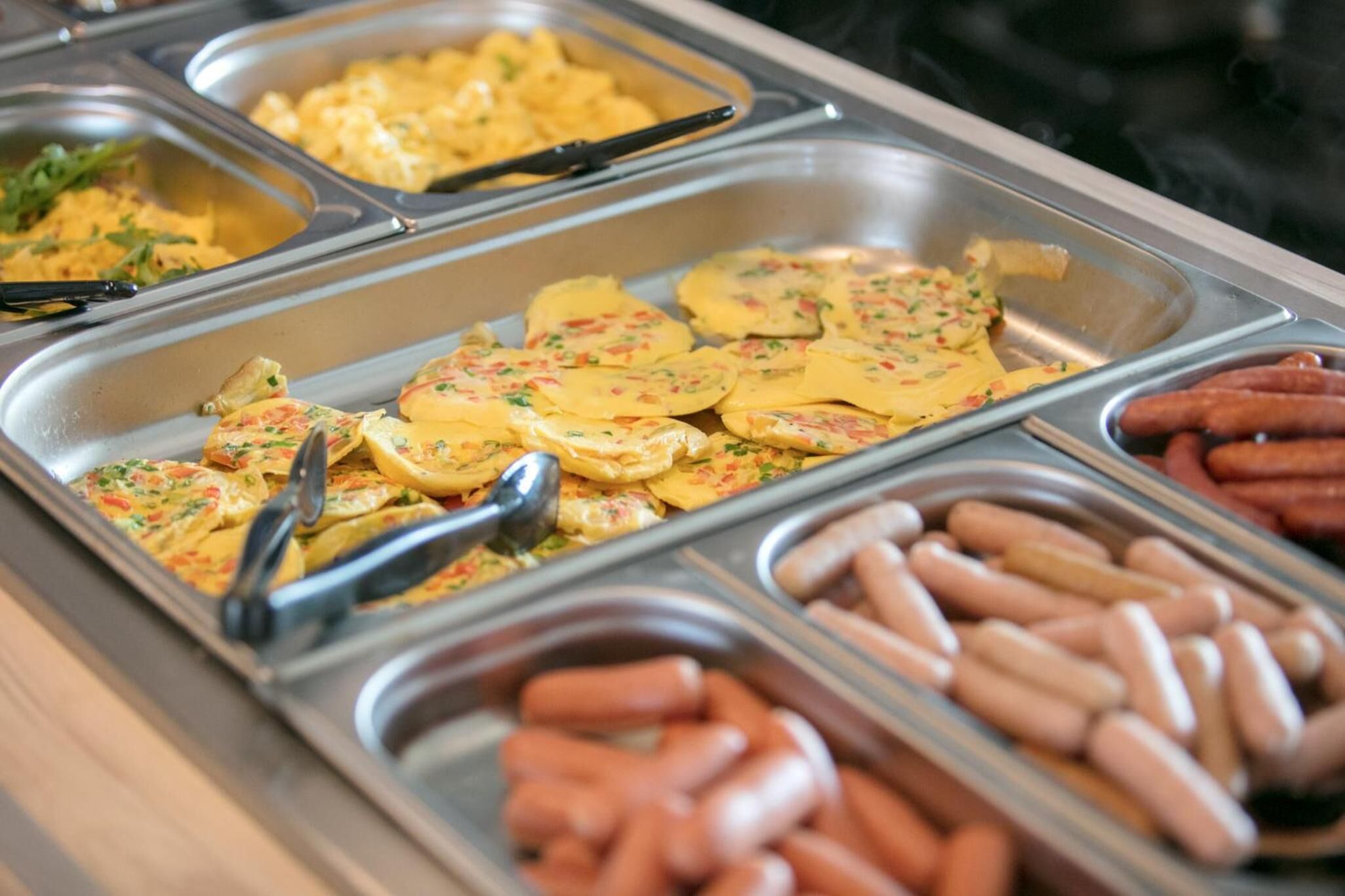 A buffet with various food items including sliced potatoes, sausages, and scrambled eggs.
