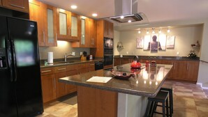Une cuisine moderne avec des meubles en bois, un réfrigérateur noir, un plan de travail en granit et une bouilloire rouge.