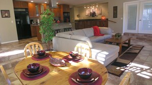 Une cuisine moderne avec des meubles en bois, un réfrigérateur noir et un coin repas doté d’une table ronde prévue pour quatre personnes.