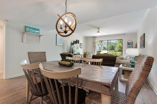 A dining area with a wooden table and chairs, a wicker bench, and a 'Beach' sign on the wall.