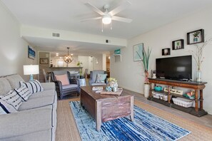 A spacious living room with a ceiling fan, a flat-screen TV, a coffee table, and a sofa.