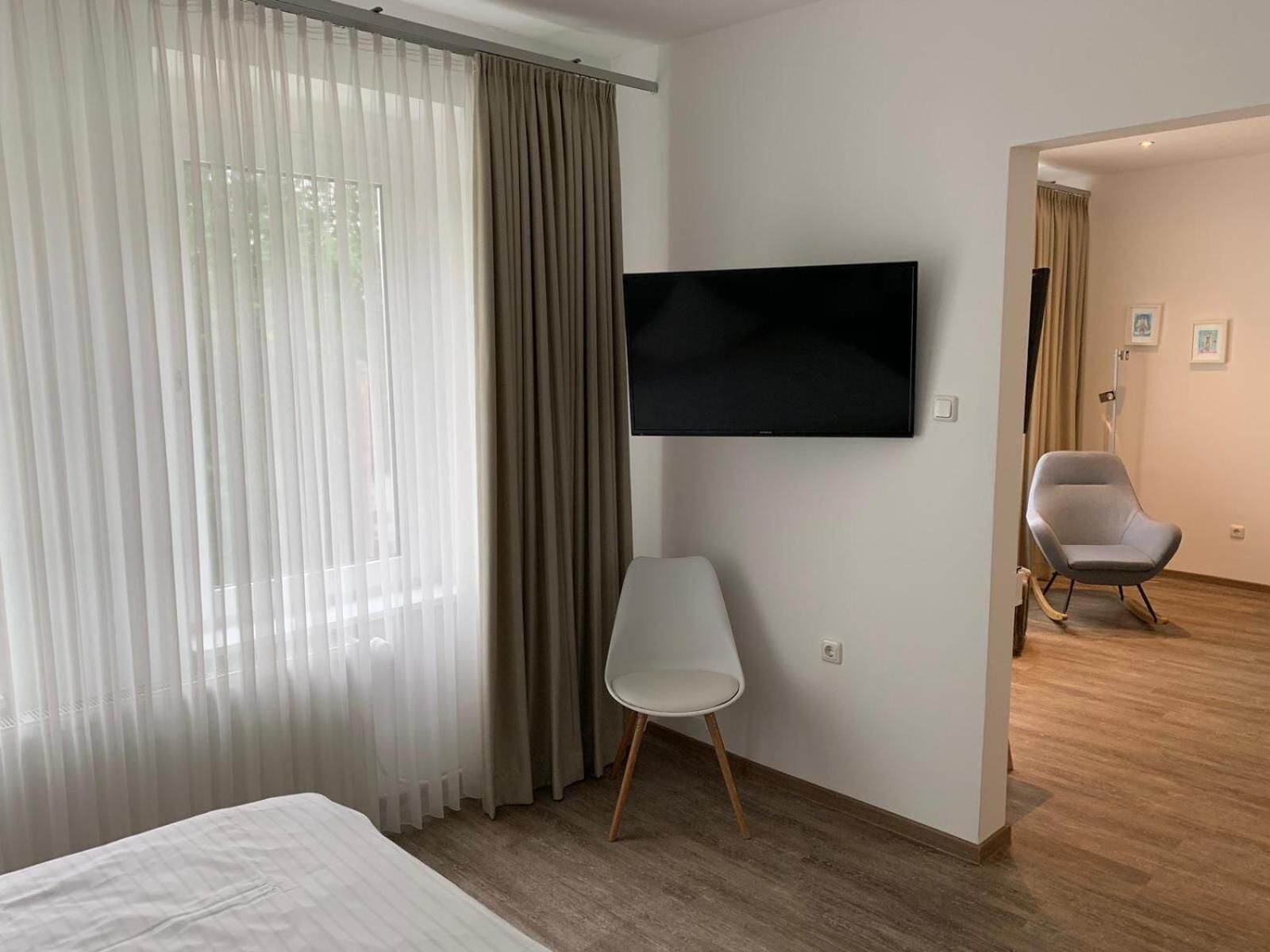 Ein modernes Hotelzimmer mit einem Bett, einem flachbildfernseher an der Wand, einem weißen Stuhl und Holzboden.